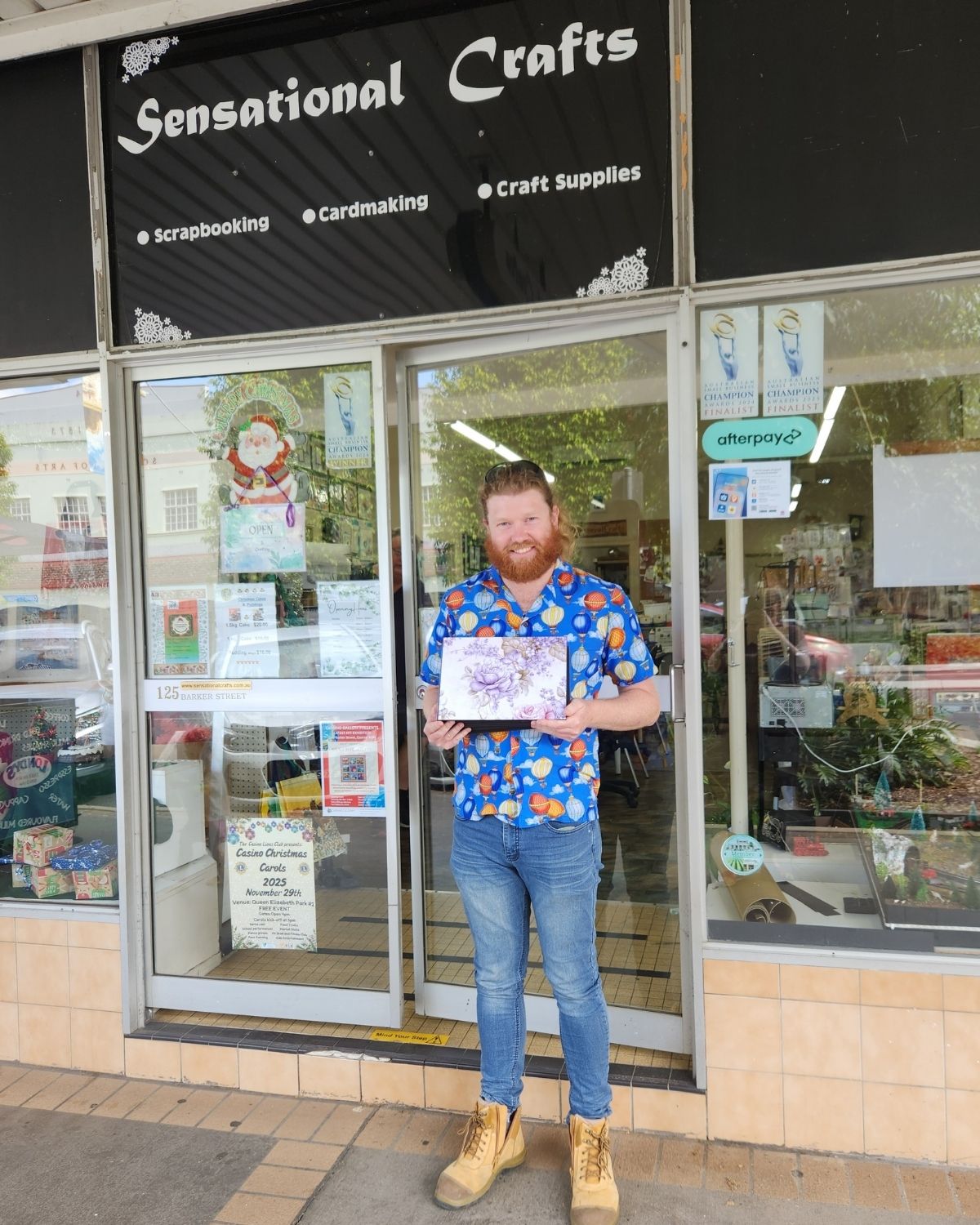 Tim holding his handmade anniversary mini album in front of Sensational Crafts, after completing the project during his lunch breaks.