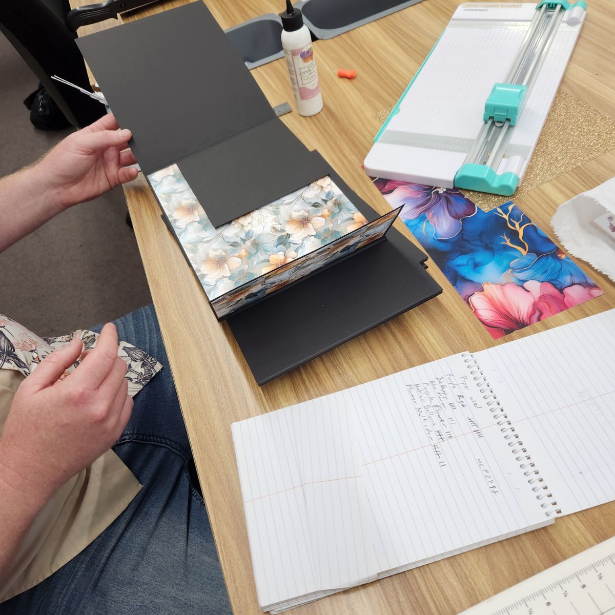 A close-up of Tim planning his mini album, with a notepad full of measurements and page layouts beside his craft supplies.